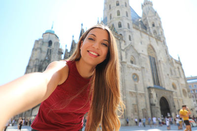 Smiling tourist woman taking a selfie with vienna cathedral on the background in austria, europe