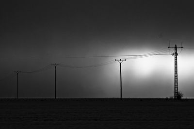 Silhouette electricity pylon by sea against sky