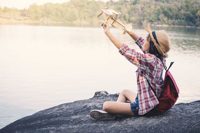 Side view of girl holding wooden airplane on rock by lake