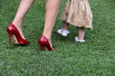 Low section of woman with daughter walking on grassy field