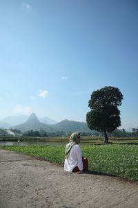 Rear view of woman sitting on field against sky