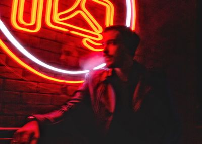 Young man sitting in illuminated sign at night