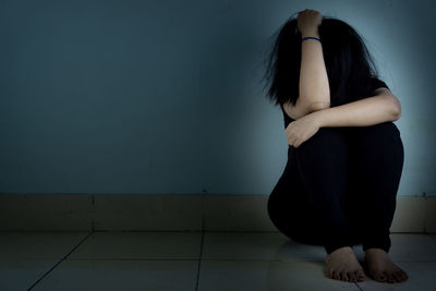 Woman sitting on tiled floor against wall at home