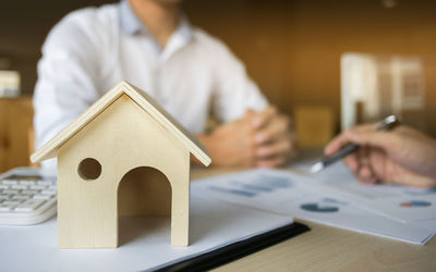 Close-up of wooden model home with businessmen discussing at desk