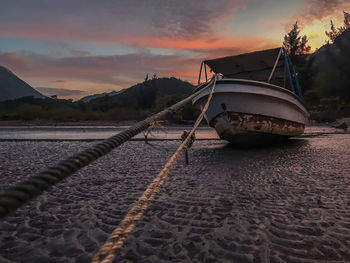 Boat moored on shore against sky during sunset