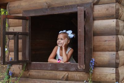 Thoughtful smiling girl looking through window in log cabin