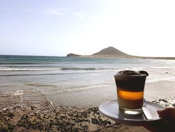 Close-up of drink on table at beach against sky