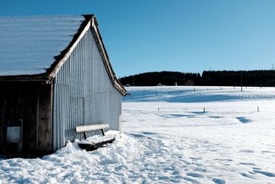 Abandoned barn on snow field against clear blue sky