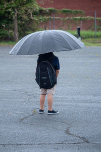 Rear view of woman with umbrella walking on wet rainy season