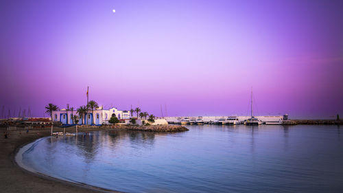 House at beach by moored boats against clear sky