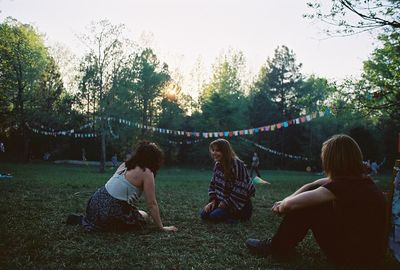 Women sitting on field by trees against sky