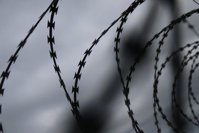 Close-up of barbed wire fence against sky