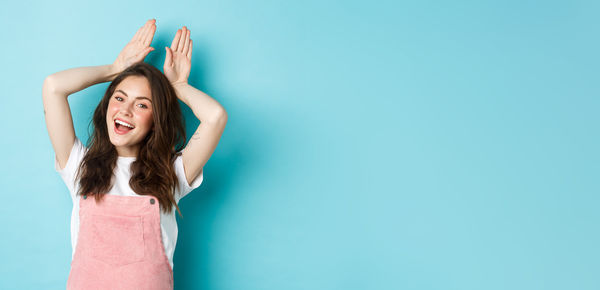 Young woman with arms raised standing against blue background