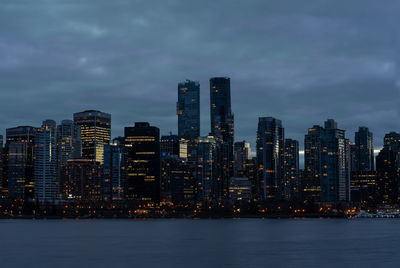 Illuminated buildings by sea against sky