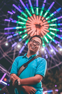 Portrait of smiling young man against illuminated ferris wheel
