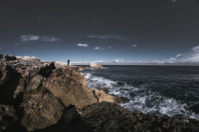 Man fishing on rock in sea against sky