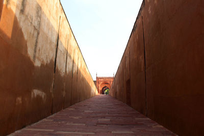 Man walking on footpath amidst buildings against sky