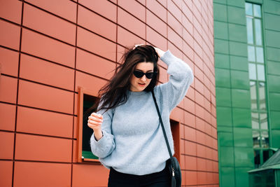 Young woman wearing sunglasses standing against wall