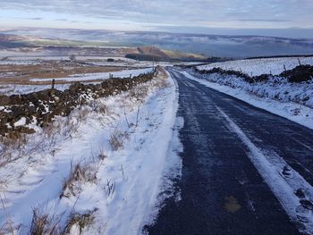Road amidst snowcapped landscape against sky