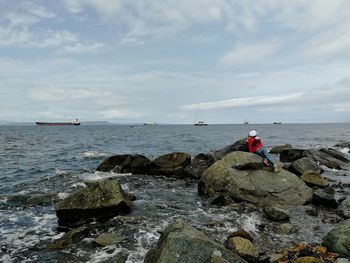 Rear view of girl on rock by sea against sky