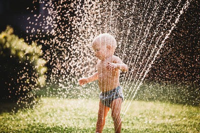 White baby standing in garden playing with water from the sprinkler