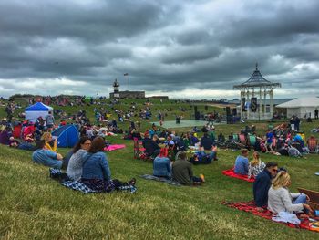 People sitting on field against cloudy sky