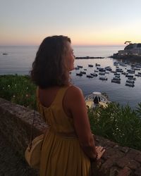 Rear view of woman looking at sea against sky during sunset