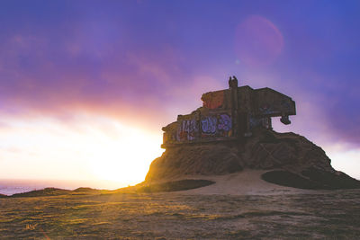 Cross on rock against sky during sunset