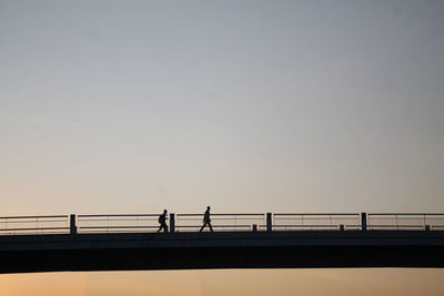 Side view of silhouette people walking on bridge against clear sky