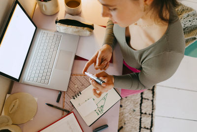 High angle view of young woman using glucometer while doing homework at table