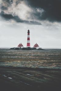 Lighthouse on grassy field against cloudy sky