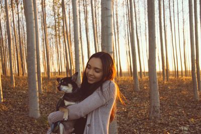 Smiling young woman carrying dog at forest