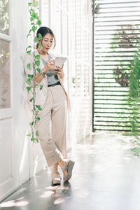 Young woman using phone while standing on wall