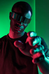 Concentrated young african american male millennial in casual clothes and vr glasses reaching out hand toward camera against green background