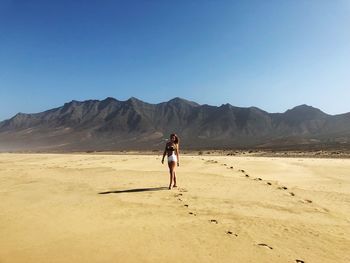 Full length of young woman standing on sand in desert against clear sky