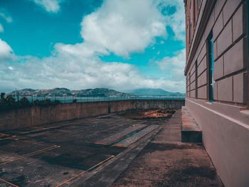 Empty road by buildings in city against sky