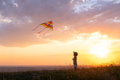 Happy little kid boy having fun with kite in nature at sunset