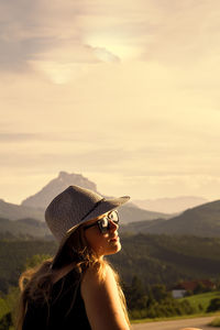 Beautiful woman wearing sunglasses and hat during sunset