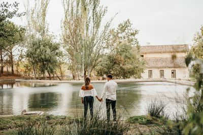 Rear view of friends standing by lake against trees