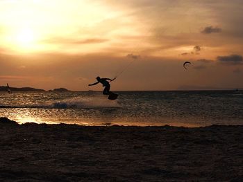 Silhouette man jumping on beach against sky during sunset