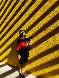 Portrait of woman wearing sunglasses standing against yellow wall