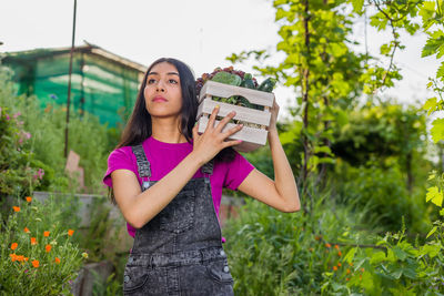 Young woman carrying crate against plants