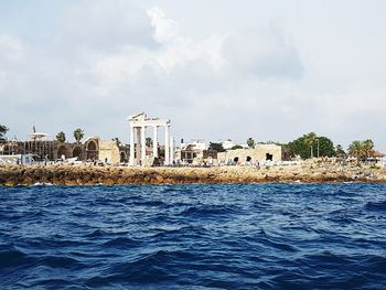 Buildings by sea against cloudy sky