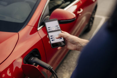 High angle view of man using app on smart phone near electric car