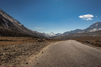 Road leading towards mountains against blue sky