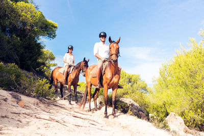 People riding horses on field against sky