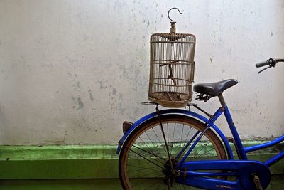 Birdcage on bicycle parked by wall