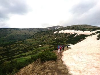 Rear view of people walking on mountain against sky