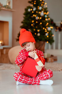 Cute girl sitting on christmas tree at home