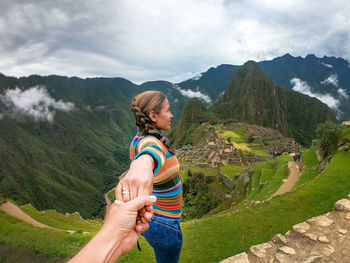 Woman holding man hand on mountain against sky